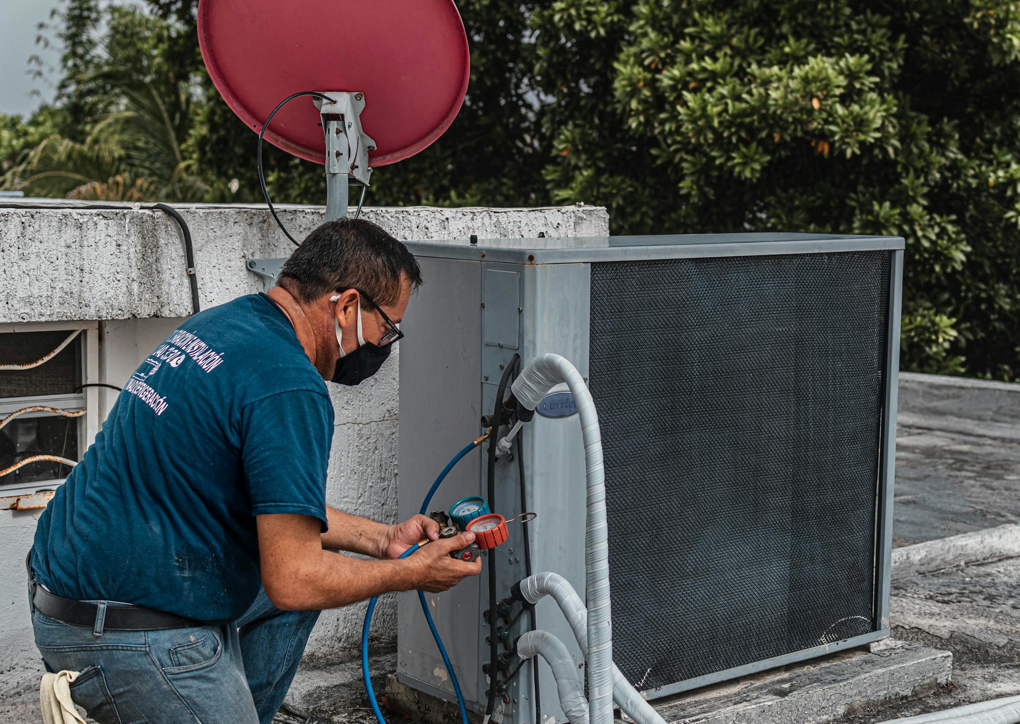 Technician in Provo diagnosing an air conditioner unit outdoors, wearing a facemask and using a manifold gauge.